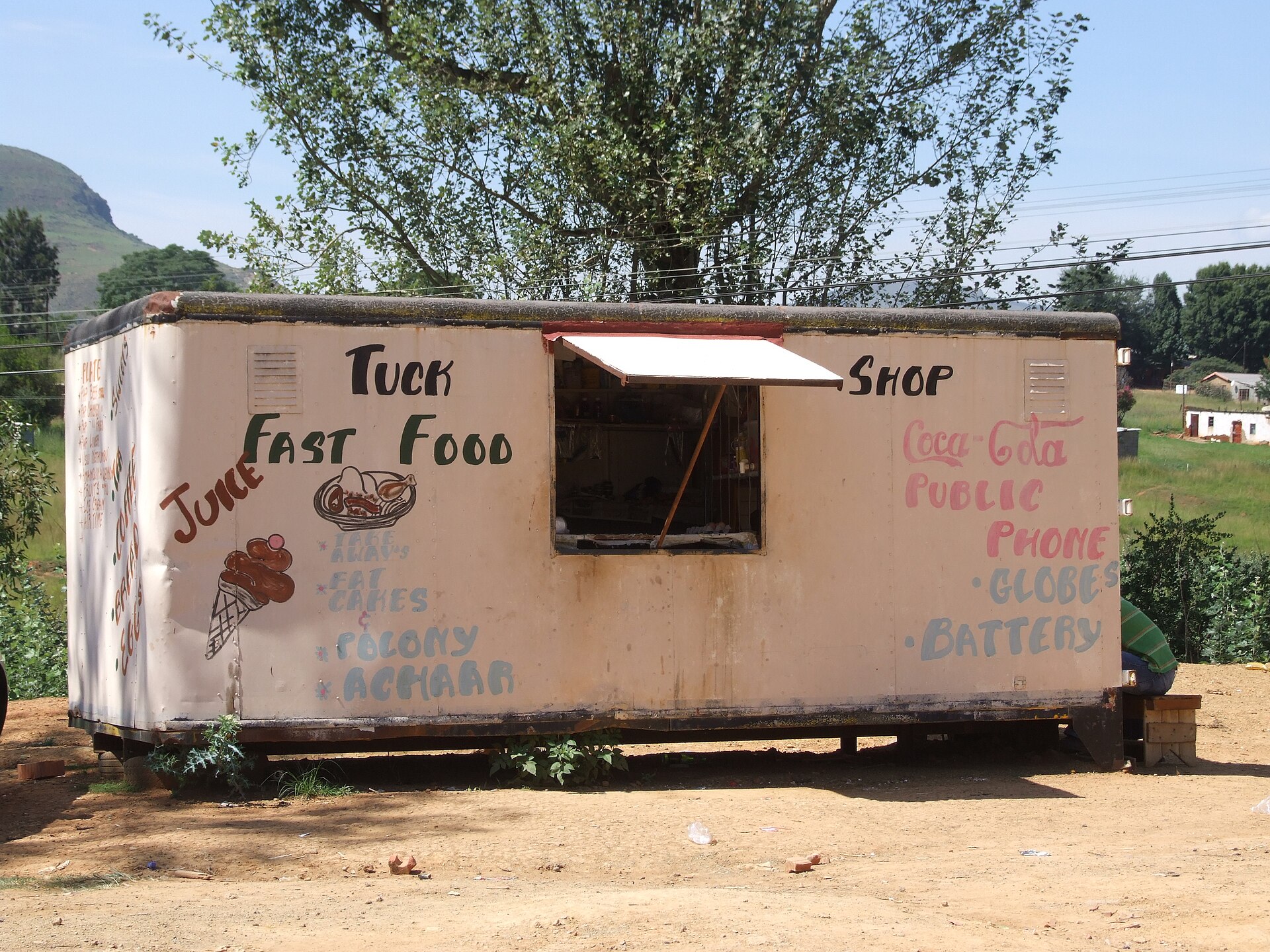 A small metal tuck shop at Cathedral Peak, KwaZulu-Natal, with one window and a door and goods advertised on the wall.